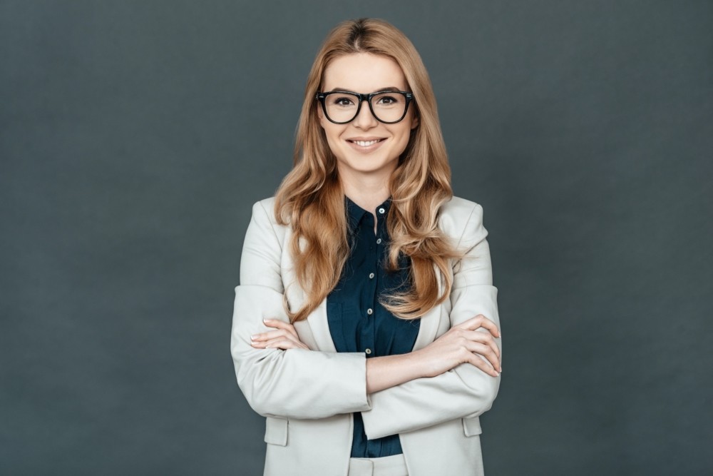 Always perfect. Gorgeous woman in smart casual wear keeping arms crossed and looking at camera while standing against grey background