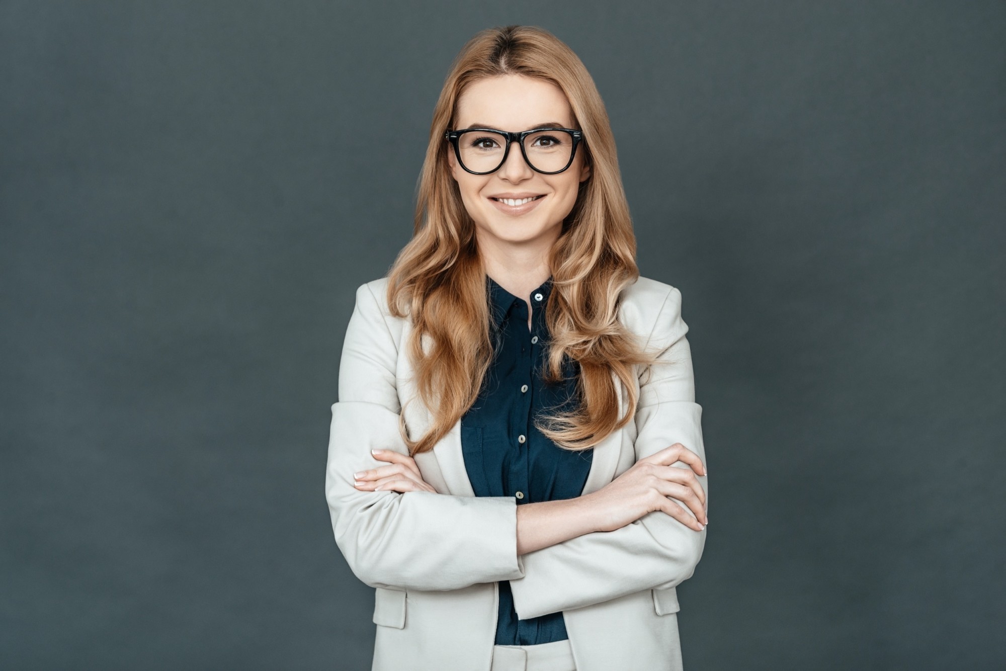 Always perfect. Gorgeous woman in smart casual wear keeping arms crossed and looking at camera while standing against grey background