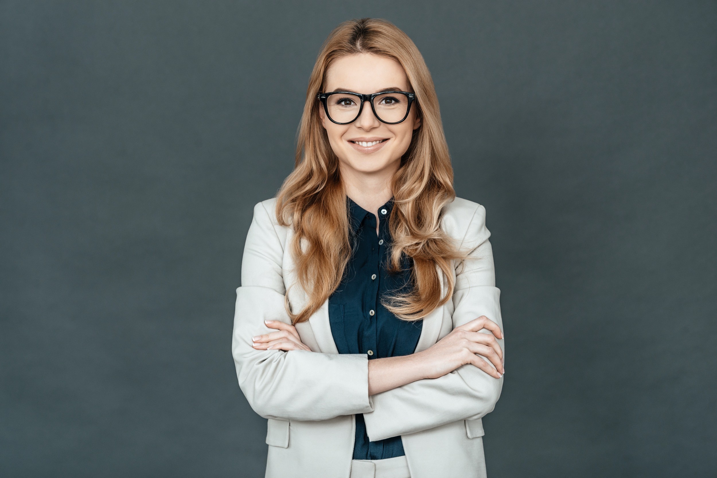 Always perfect. Gorgeous woman in smart casual wear keeping arms crossed and looking at camera while standing against grey background