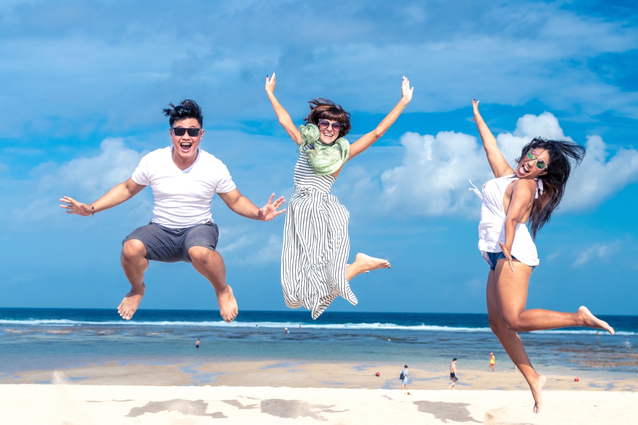 3 people who are at the beach jumping in the air laughing.