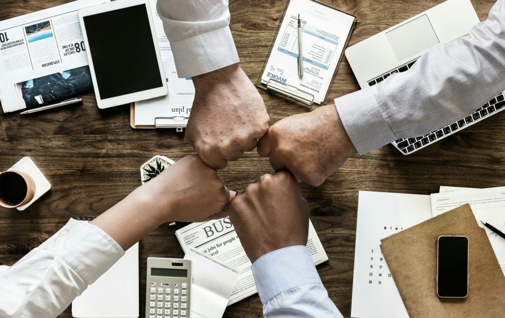 4 people giving each other a fistbump at their desk.