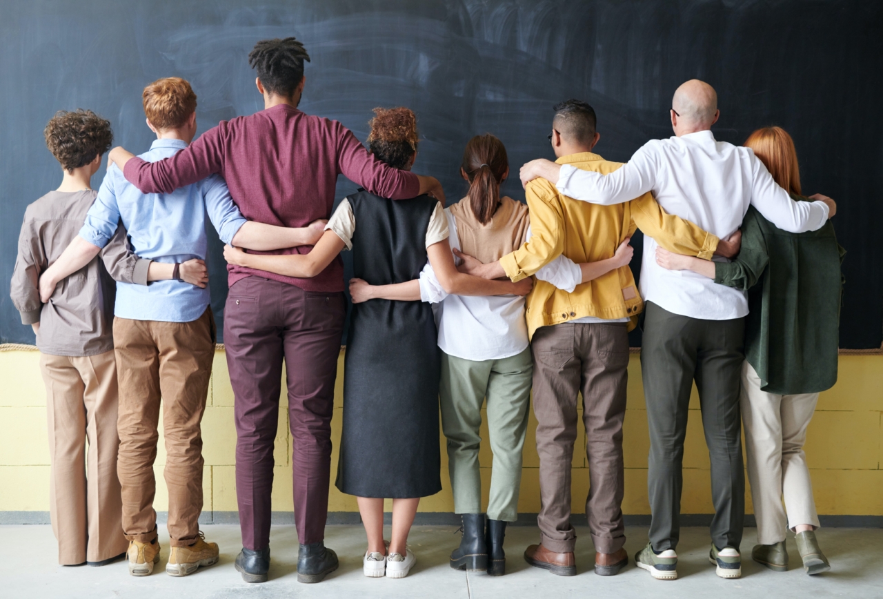 A group of people looking at a blackboard and having each other’s arm around the shoulder.