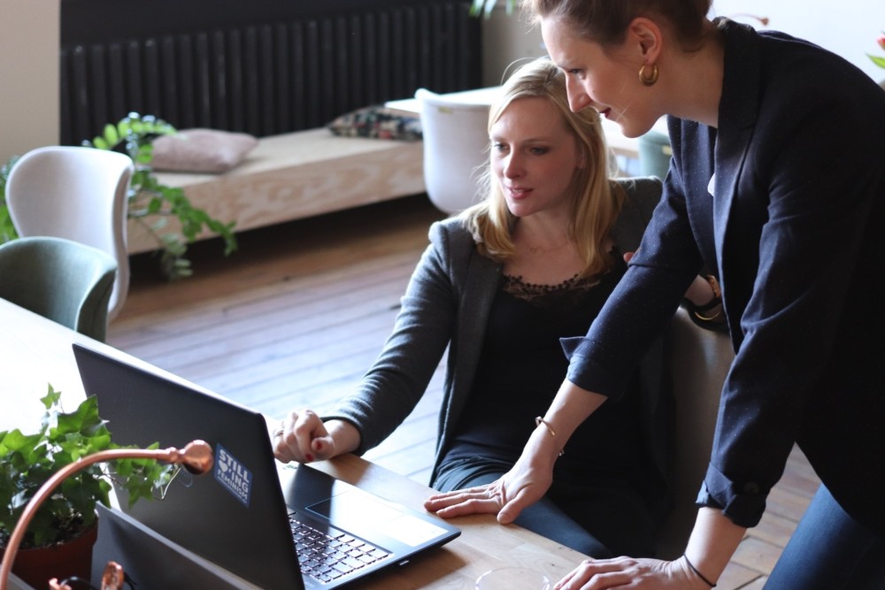 2 women looking at a laptop in some kind of open office.