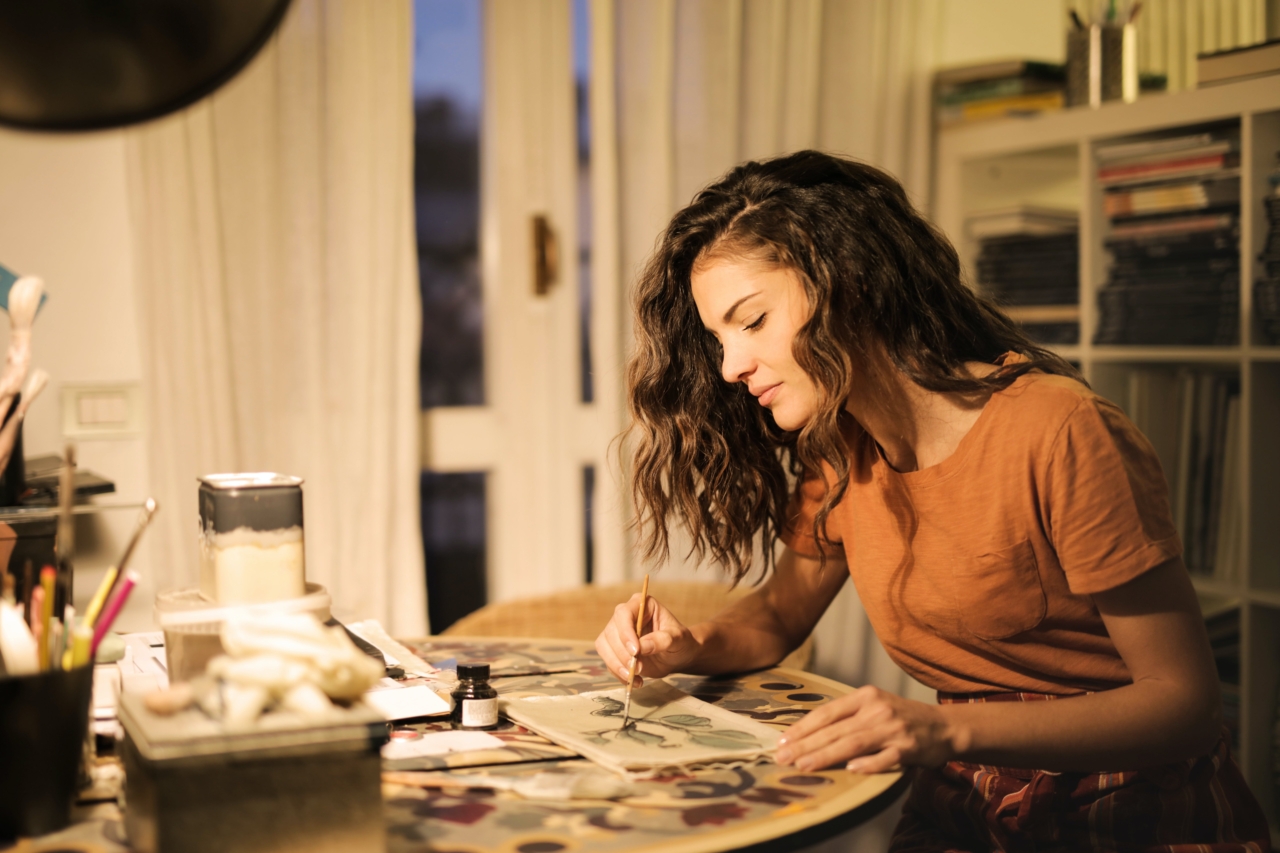 A woman sitting at a table and painting something on a piece of paper.